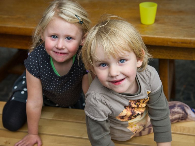 Zwei Kinder sitzen auf einer Holzbank und schauen in die Kamera.