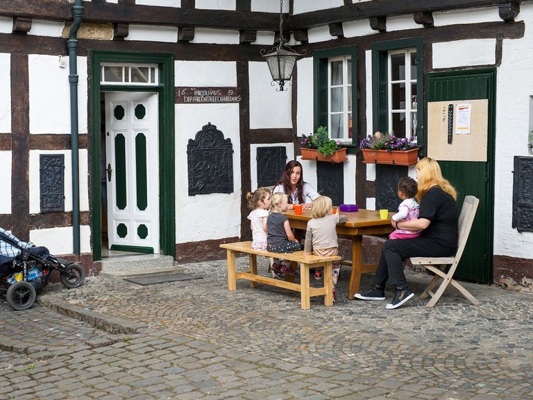 Zwei Mütter sitzen mit vier Kindern vor dem Mutter-Kind-Haus in Bonn und trinken aus bunten Bechern