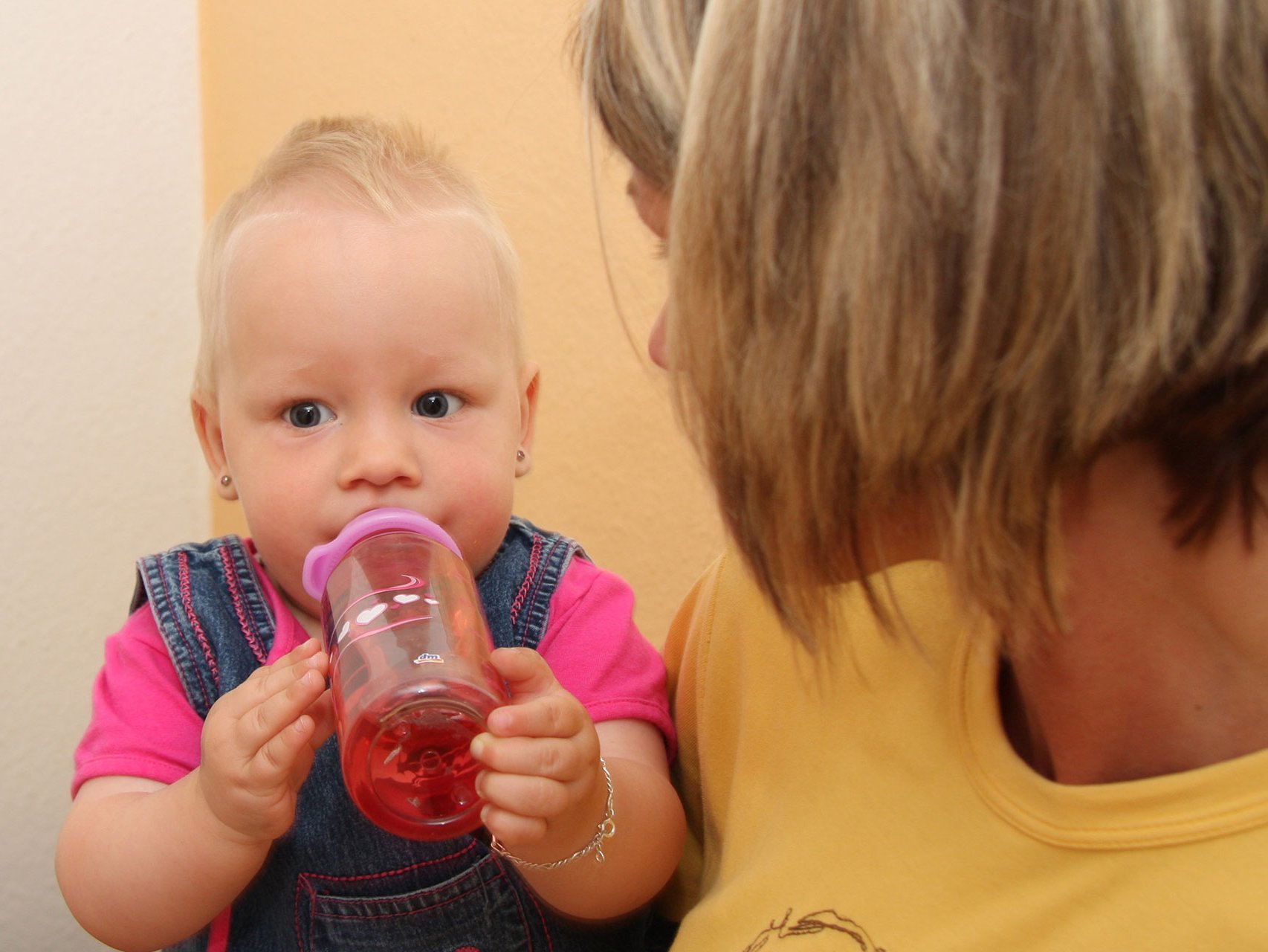 Mutter hält kleines Kind auf dem Arm, während das Kind zufrieden aus einer Flasche trinkt. 