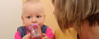 Mutter hält kleines Kind auf dem Arm, während das Kind zufrieden aus einer Flasche trinkt. 