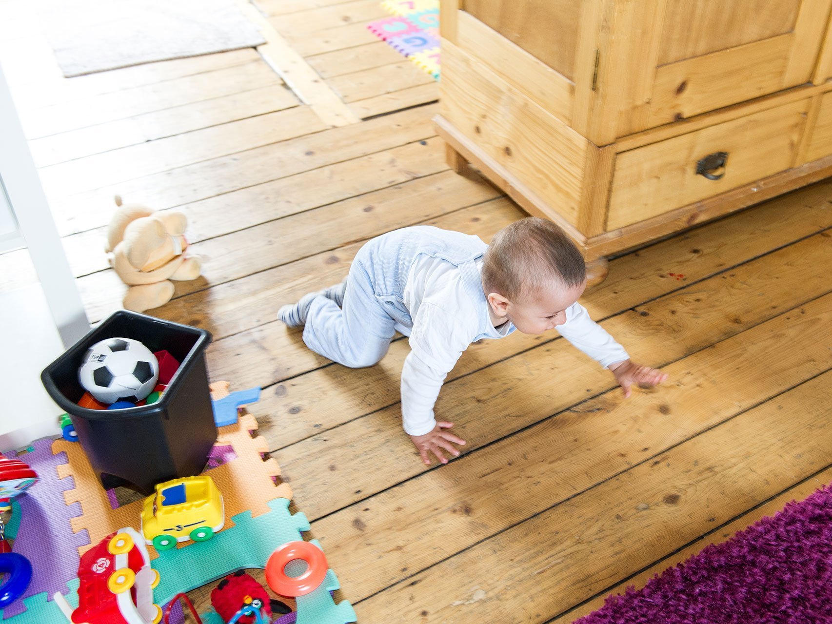 Kleines Kind krabbelt auf dem Holzboden und neben dem Kind liegt Spielzeug